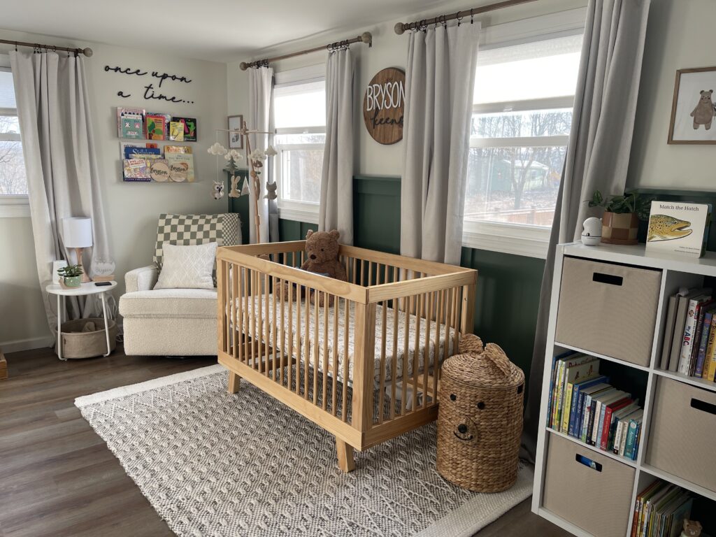 Photo of a woodland themed baby nursery with a light natural wooden crib, beige rocking chair, and area rug. 