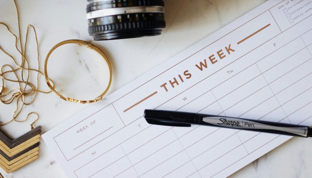 Break through the overwhelm with a calendar. A calendar with a pen on top of it with jewelry around it