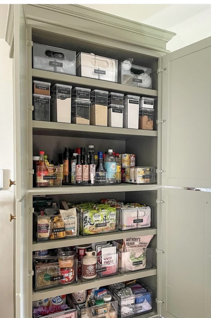 A cabinet pantry with pantry items stored in clear bins.