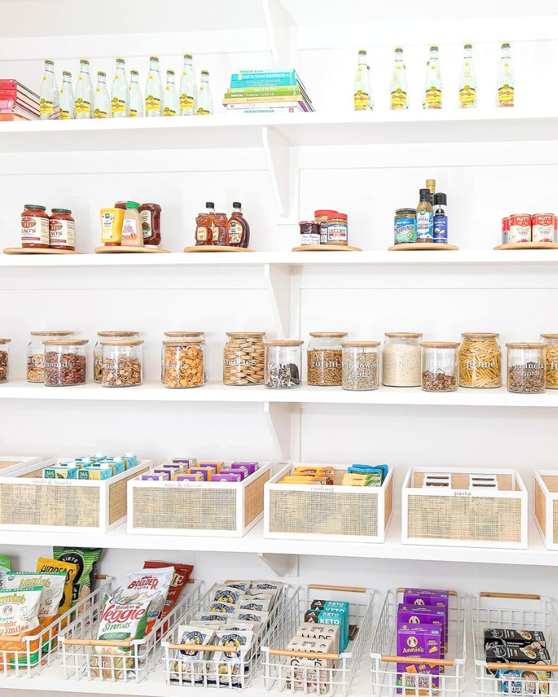White pantry with shelving organized with pantry items in jars, decorative bins, lazy susans, and wire baskets.