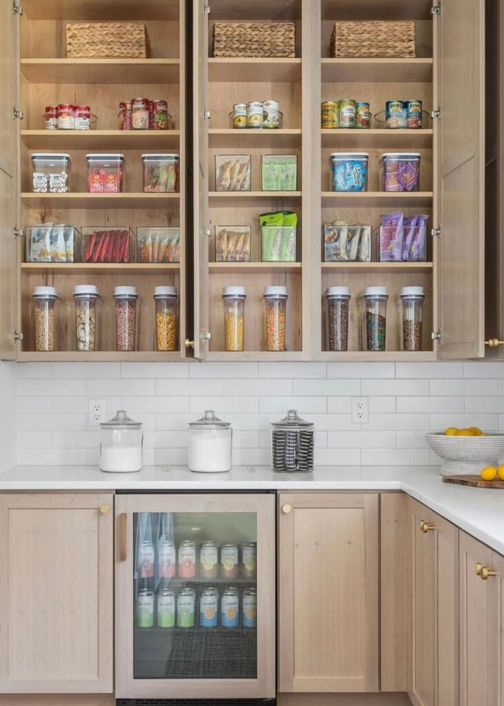 Large light wood cabinet pantry organized with plastic containers, wicker baskets, and a mini refridgerator.