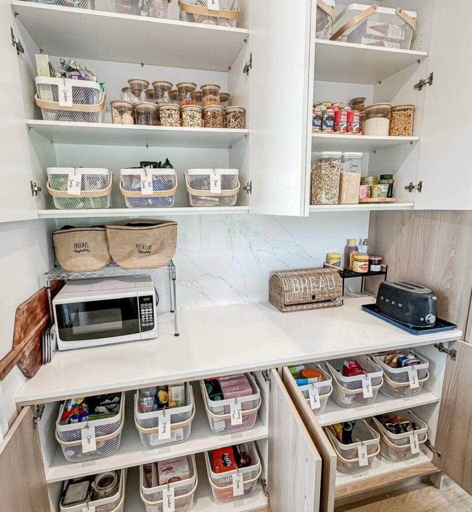 A white cabinet pantry organized with white wire baskets, jars, and labels.