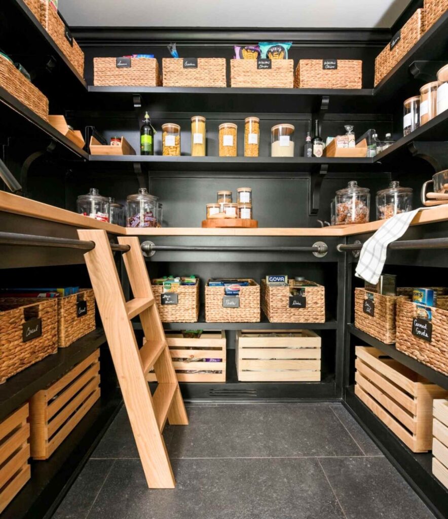 Farmhouse black pantry with woven baskets, glass jars, crates, a ladder, and pantry staples.