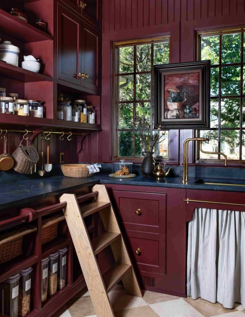 Burgundy color country pantry with a rolling ladder, sink, shelving, cabinets, sink, and a painting.