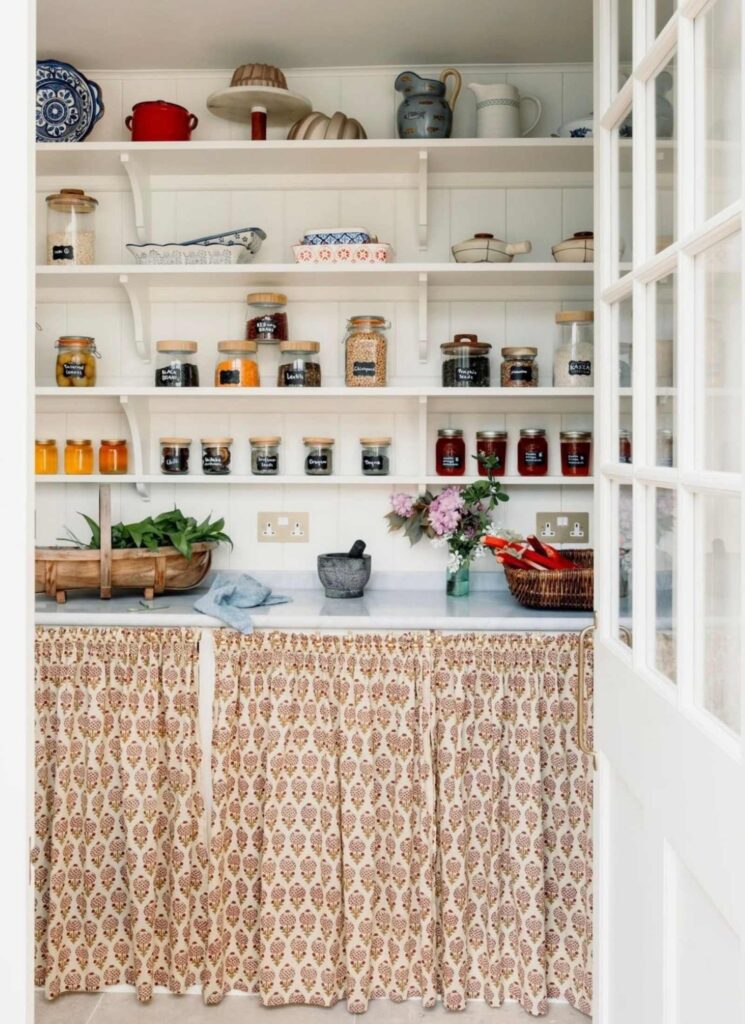 Country pantry with open shelving with jars, bowls, serving trays, baskets on the shelving.