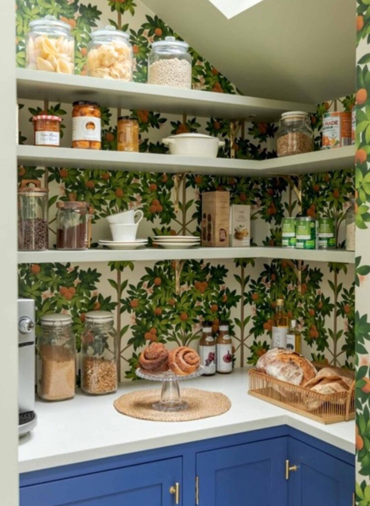 Farmhouse pantry with wallpaper, shelving, pantry items, and blue cabinets.