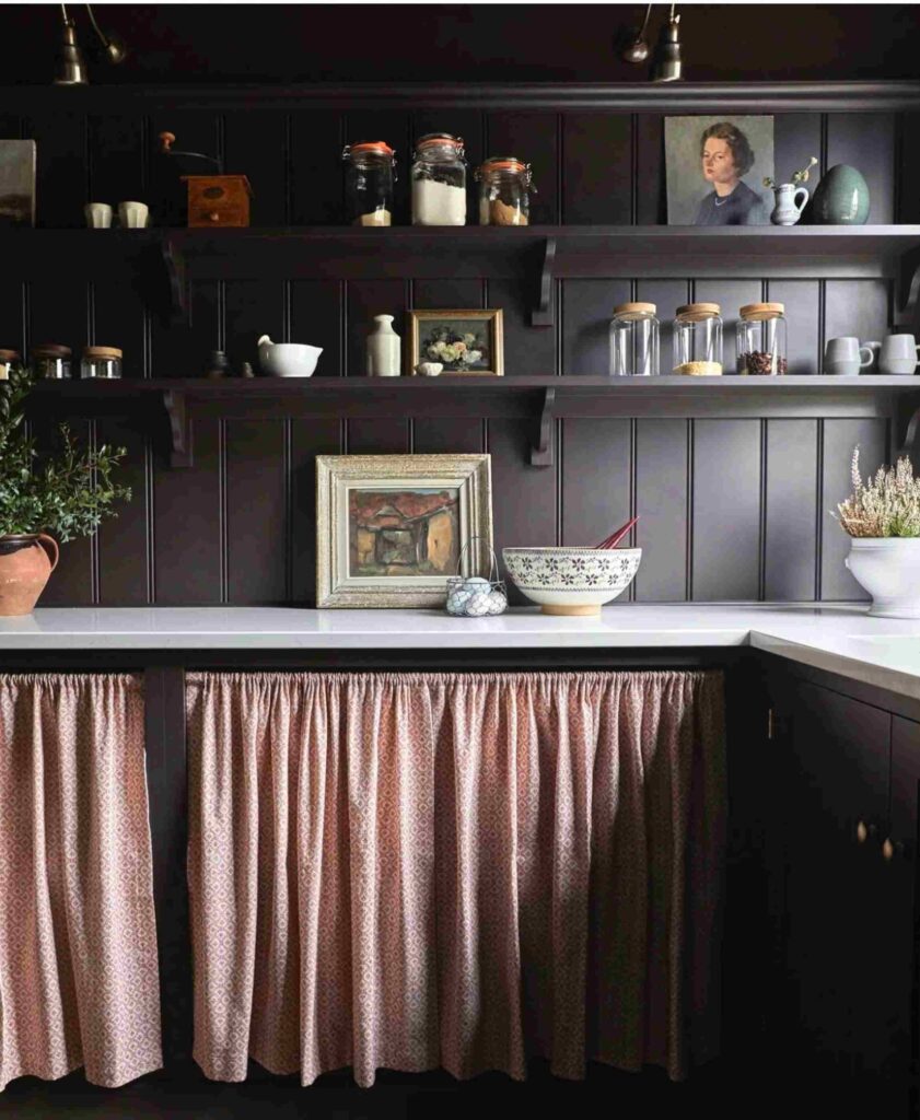 Country pantry painted in a deep burgundy, with decor on shelves, jars, basket of eggs, plants, and pantry curtain.