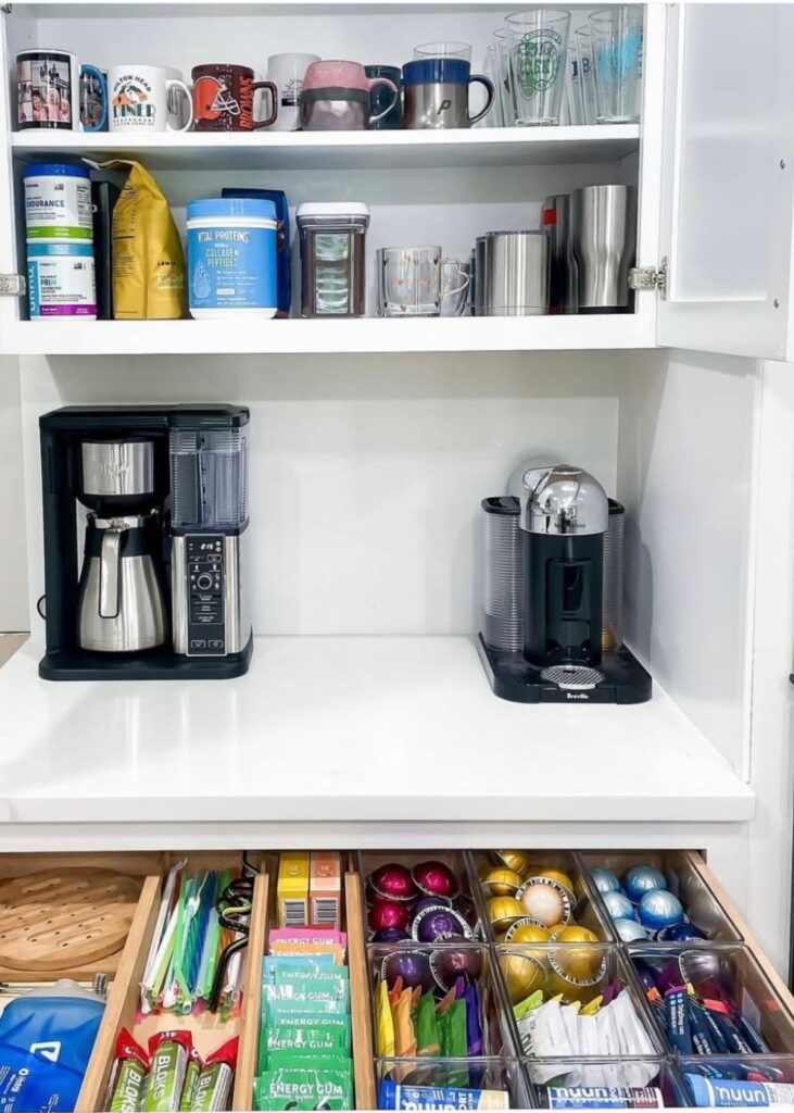 Kitchen cabinet and drawer organized with a coffee maker, coffee mugs, coffee pods, tea, energy drinks, and glass cups 