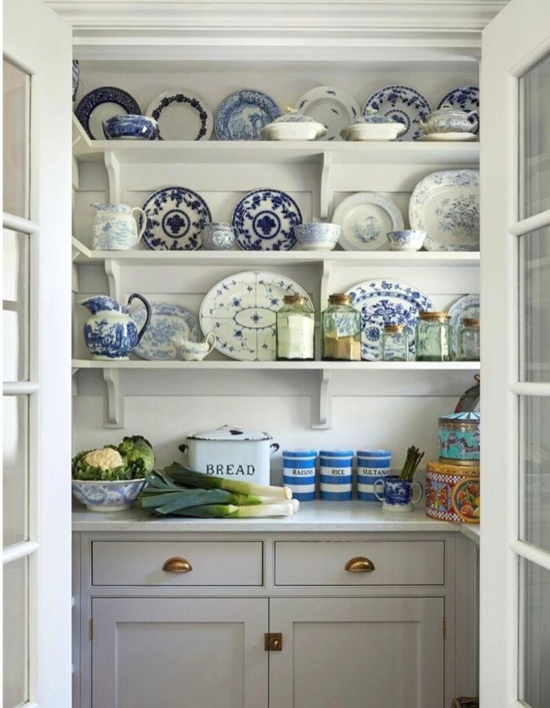 Country white pantry with open shelving with pretty dinnerware displayed on the shelves, jars, and produce.