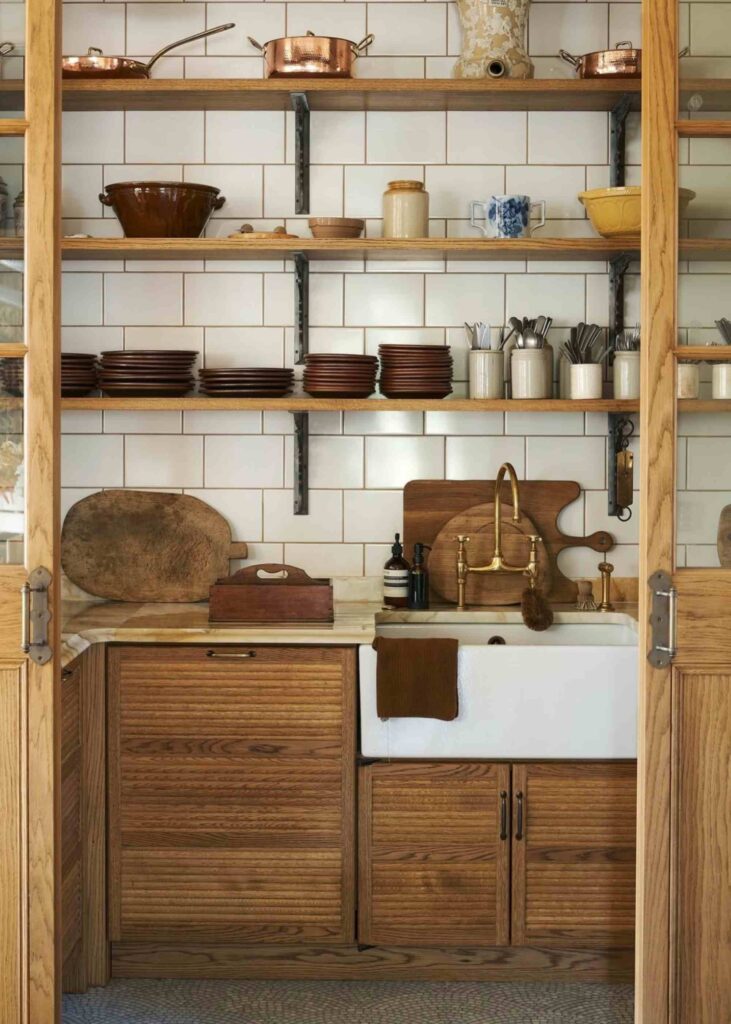 A picture of a farmhouse kitchen pantry with a sink, wood shelving, wood cutting boards, plates, utensils, and bowl decor.