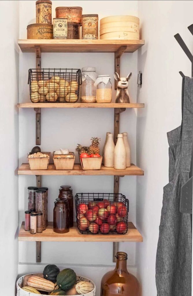 Country pantry created on open shelving, with country inspired decor such as vintage tins, wire baskets, ball jars, and fruit baskets.