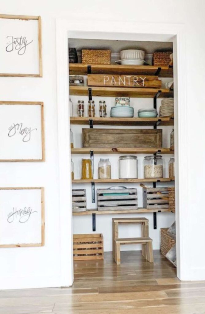 Farmhouse pantry decorated with different color woods bins, jars, plates, cookware, woven bins, and a wooden stepladder.