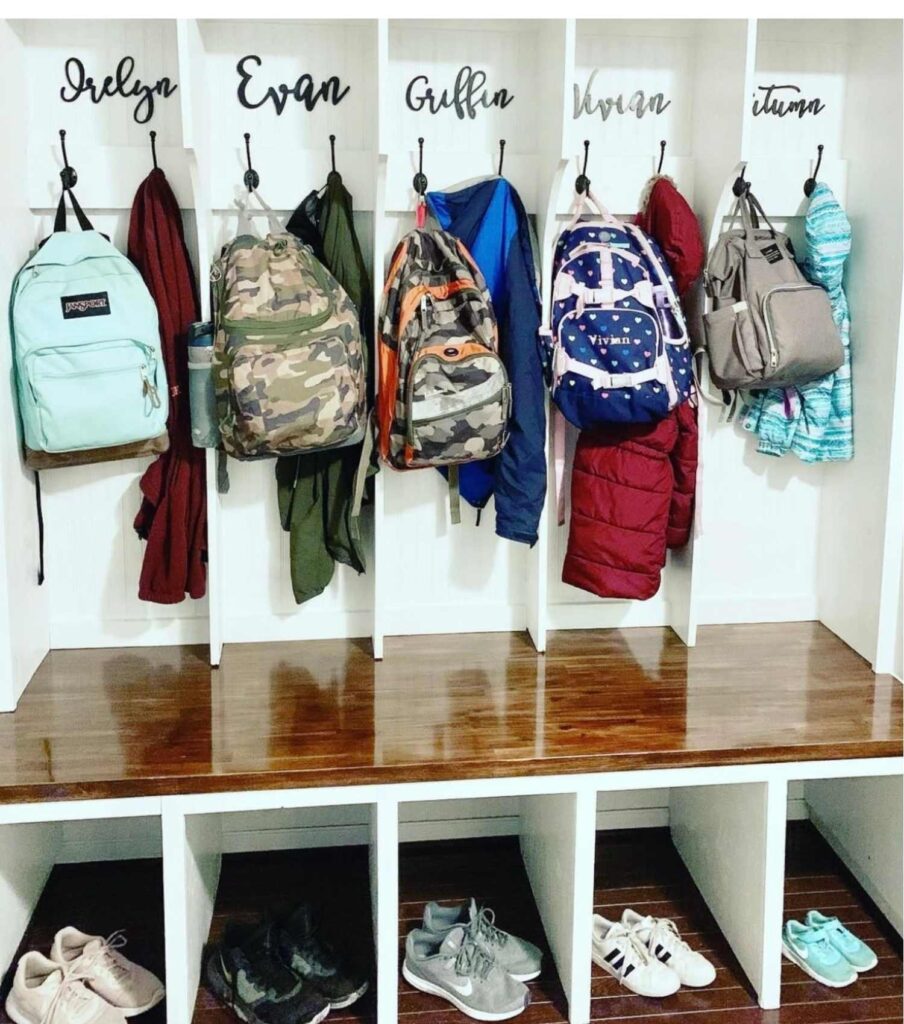 Cubbies in a mudroom with backpacks hanging on hooks, name of each child, and shoes. 