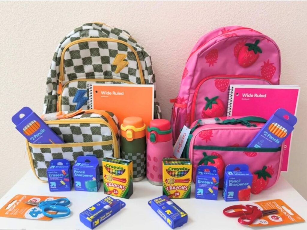 Two backpacks with school supplies in them and around them. 