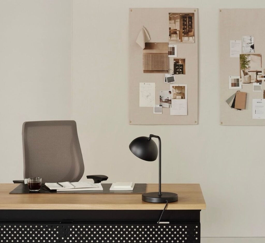 An office space with a desk and a felt board on the wall with pictures on the board. 