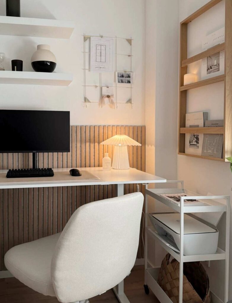 Organized desk space with a small lamp, desktop computer, wall shelving, 3-tiered floor caddy, and shelving on the wall. 