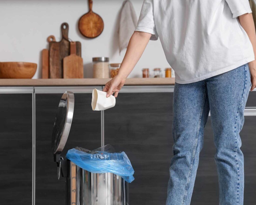 Person throwing away trash in the kitchen so there are clutter free kitchen counters. 