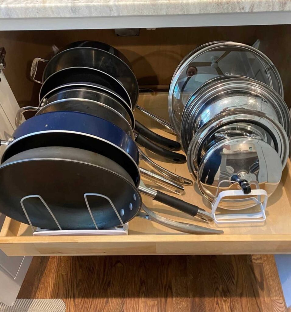 Pots and pans stored on a pullout kitchen cabinet drawers using expandable cookware racks