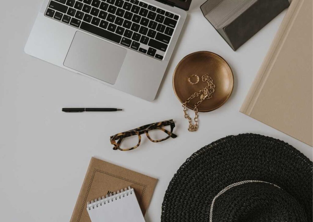 Aesthetic picture of computer, glasses, black hat, journal, at a desk. 