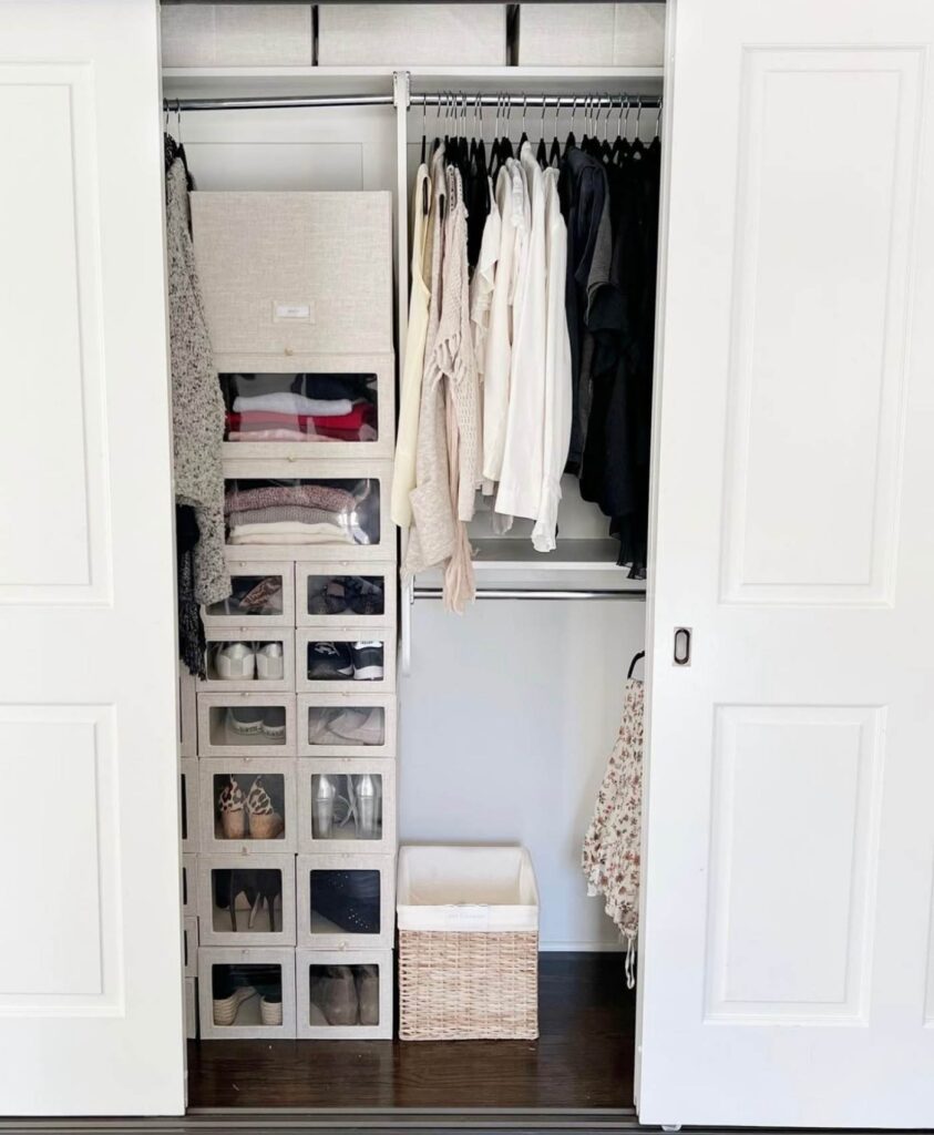 Small closet with two rods, and stackable light beige cloth boxes for shoe storage and clothes storage. 