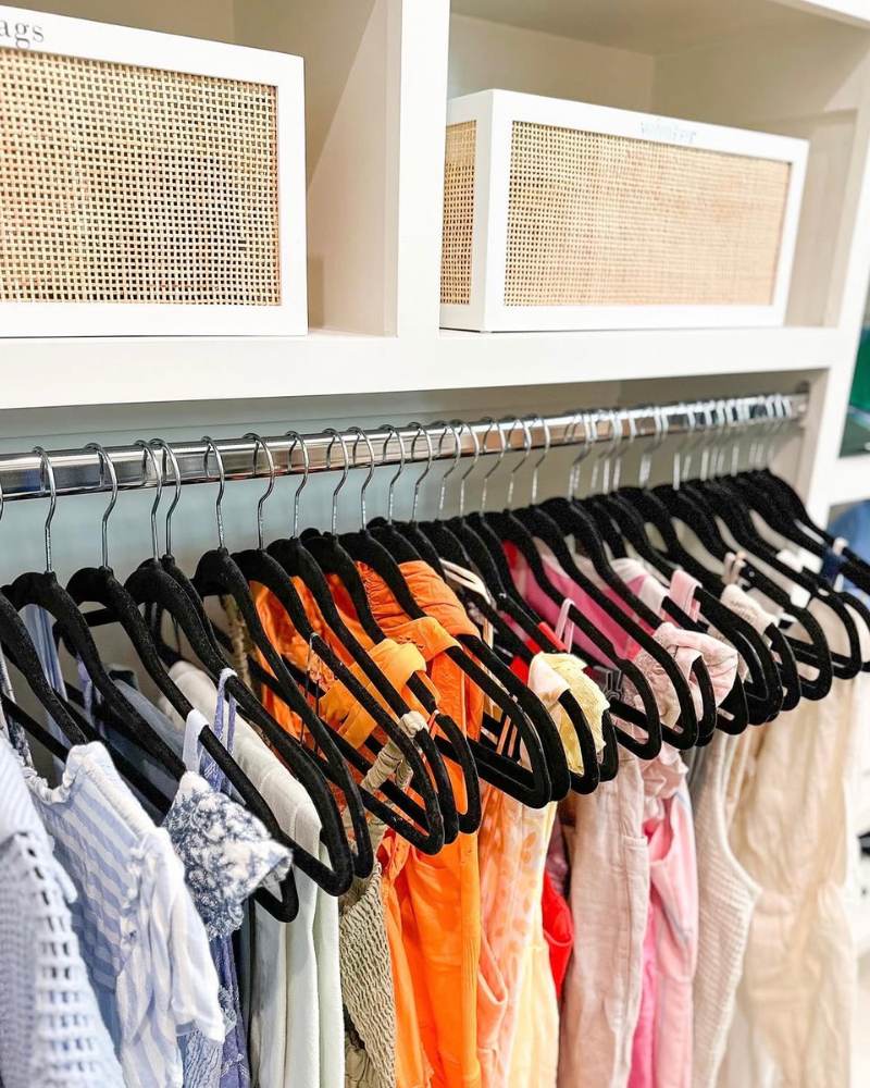 Clothes hanging on black velvet hangers in a small closet. 